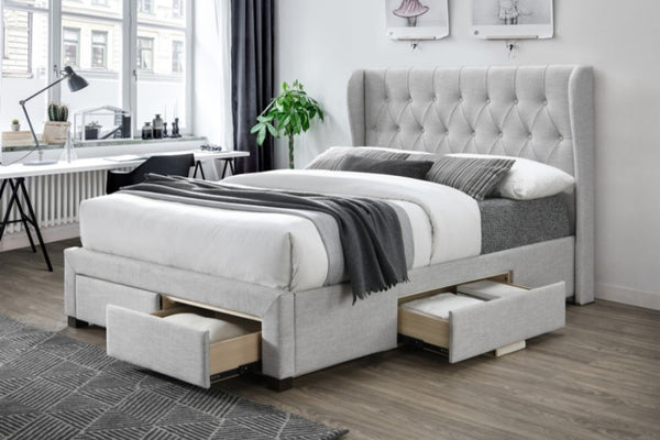 Light Grey winged and diamonded buttoned upholstered bed with storage drawers in a room with a desk and plants.