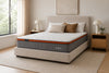Morrison Bliss mattress with signature orange band and bliss script logo, shown at an angle on an upholstered bed frame in a softly lit bedroom with natural light through sheer curtains
