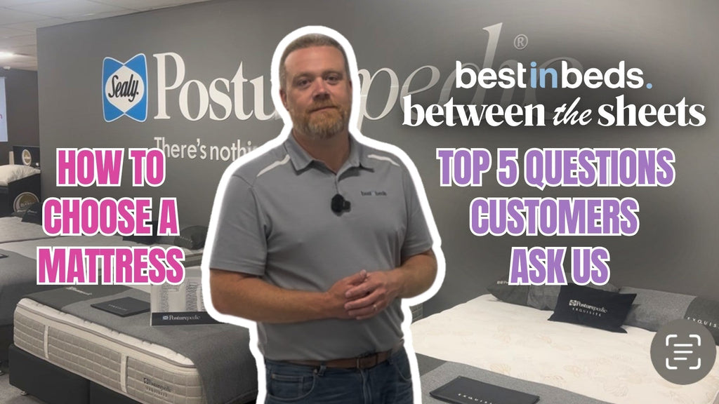 An experienced mattress expert standing in front of a Sealy Posturepedic Exquisite mattress display witha video on "how to Choose a Mattress" and "Top 5 Questions Customers Ask us"
