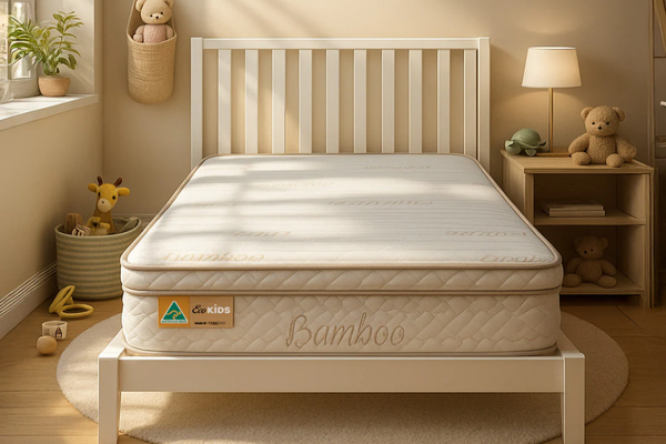 An Eco Kids Deluxe King SIngle Pillow Top Mattress pictured on a white timber bed frame with a slatted bedhead in a child bedroom setting with a teddy bear on a timber bedside table and a toy giraffe in a basket