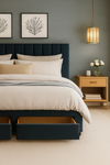 Modern bedroom with a dark blue upholstered bed, beige bedding, and a wooden nightstand.