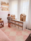 Child sitting on a wooden Boori Kids Tidy Toy Cabinet pctured in the Barley White & Almond Colour in a bright room with white curtains.