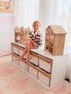 Child sitting on a wooden Boori Kids Tidy Toy Cabinet pctured in the Barley White & Almond Colour in a bright room with white curtains.