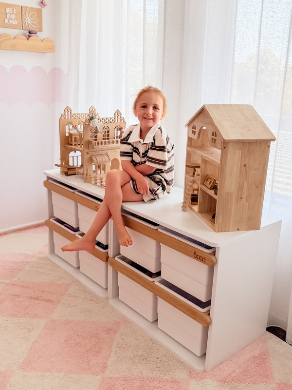 Child sitting on a wooden Boori Kids Tidy Toy Cabinet pctured in the Barley White & Almond Colour in a bright room with white curtains.